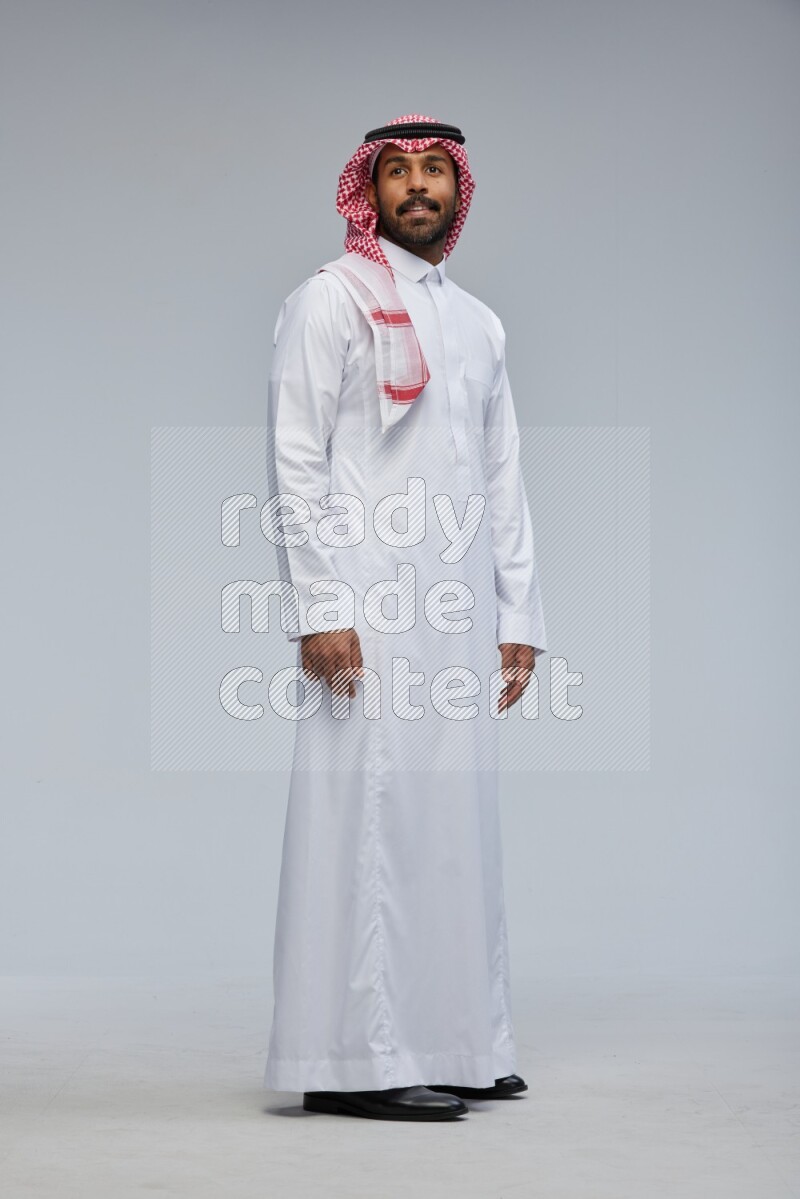 Saudi man Wearing Thob and shomag standing interacting with the camera on Gray background