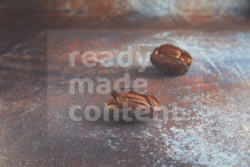 two pecan stuffed madjoul dates on a rustic reddish background
