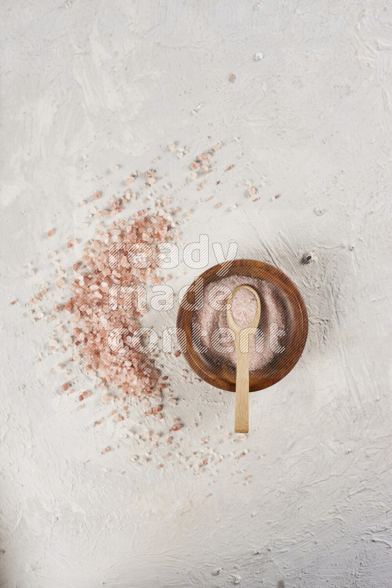 A pottery plate full of fine salt with bunch of coarse salt beside it on white background