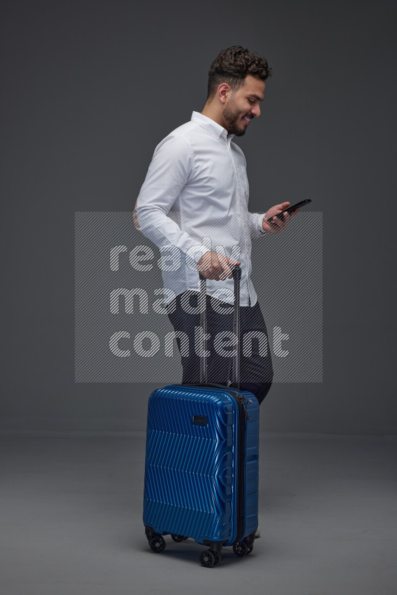 A man wearing smart casual holding luggage eye level on a gray background