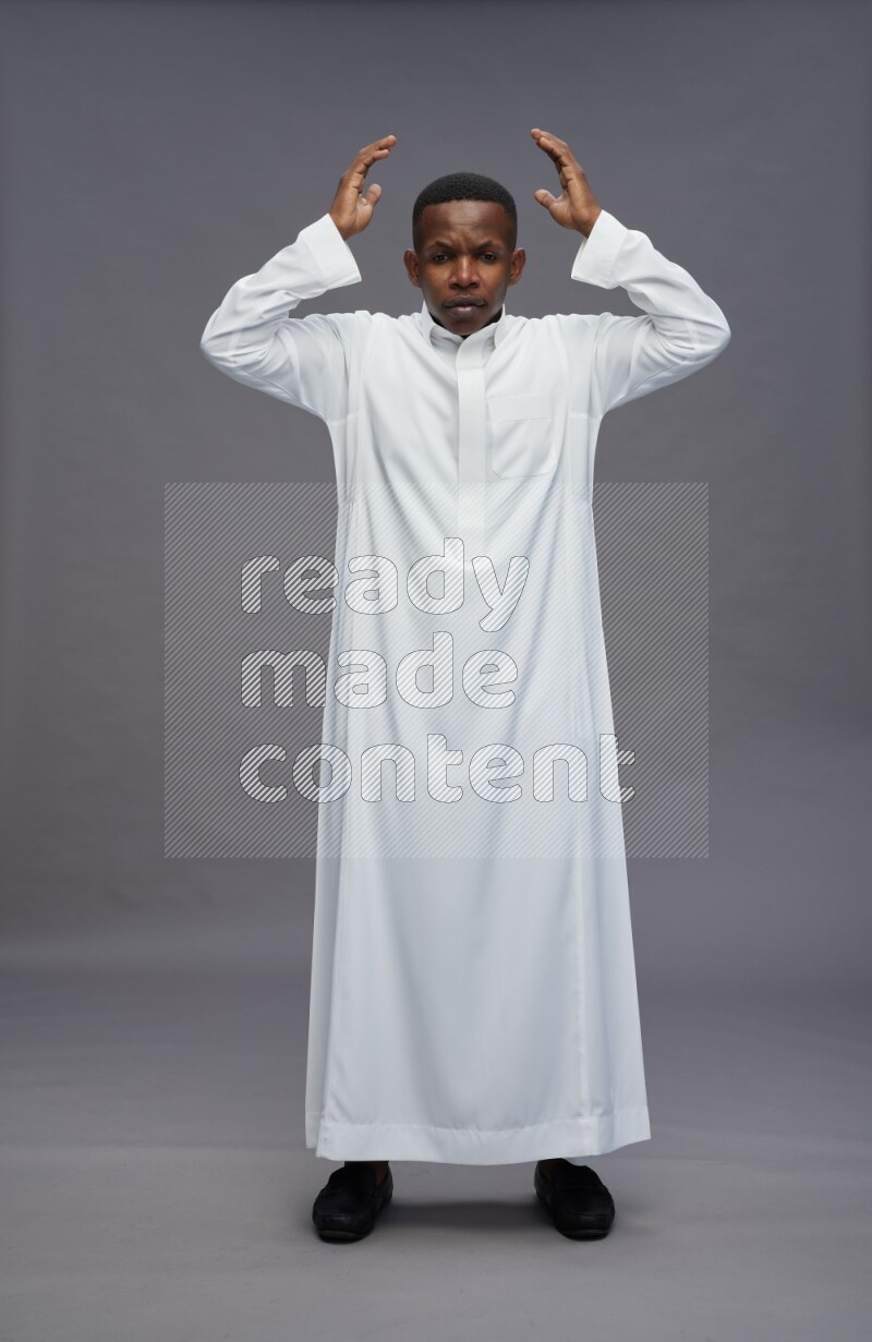 Saudi man wearing thob standing hands behind head on gray background
