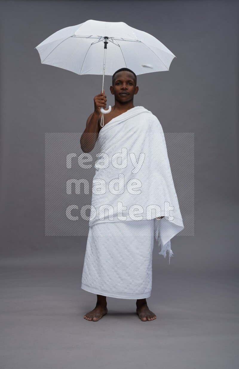 A man wearing Ehram Standing holding umbrella on gray background