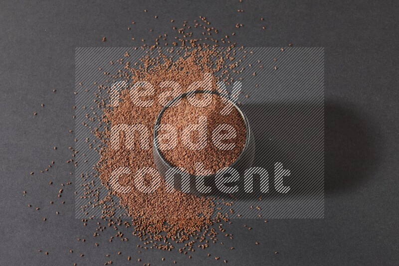 A black pottery bowl full of garden cress seeds surrounded by seeds on a black flooring