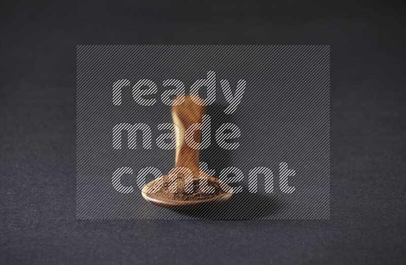 A wooden ladle full of cloves powder on a black flooring
