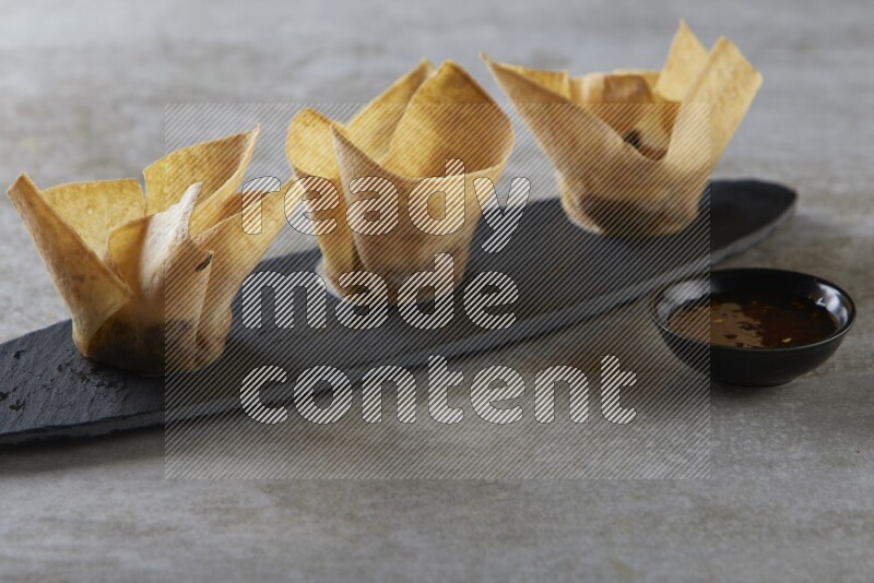 wonton cups with soy sauce ramkin on oval slate on grey textured counter top