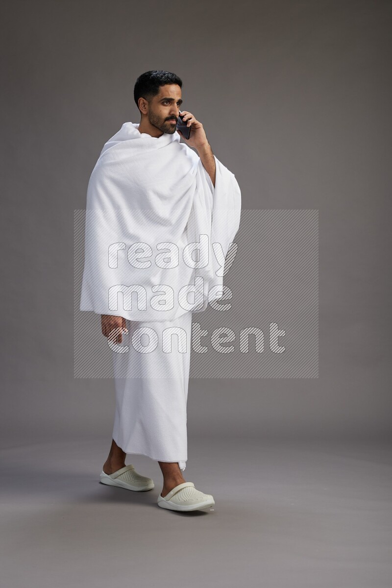 A man wearing Ehram Standing talking on phone on gray background