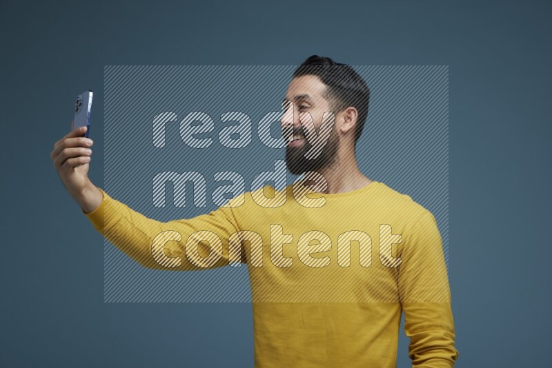 Man Taking a Selfie  in a blue background wearing a yellow shirt
