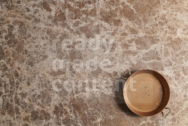 A small copper pan on beige marble background
