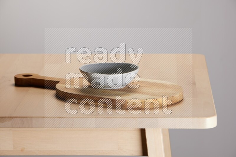 grey bowl placed on a  wooden oval cutting board on the edge of wooden table