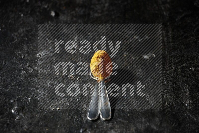 ملعقتان معدنيتان ممتلئتان ببودرة الكركم على خلفية سوداء