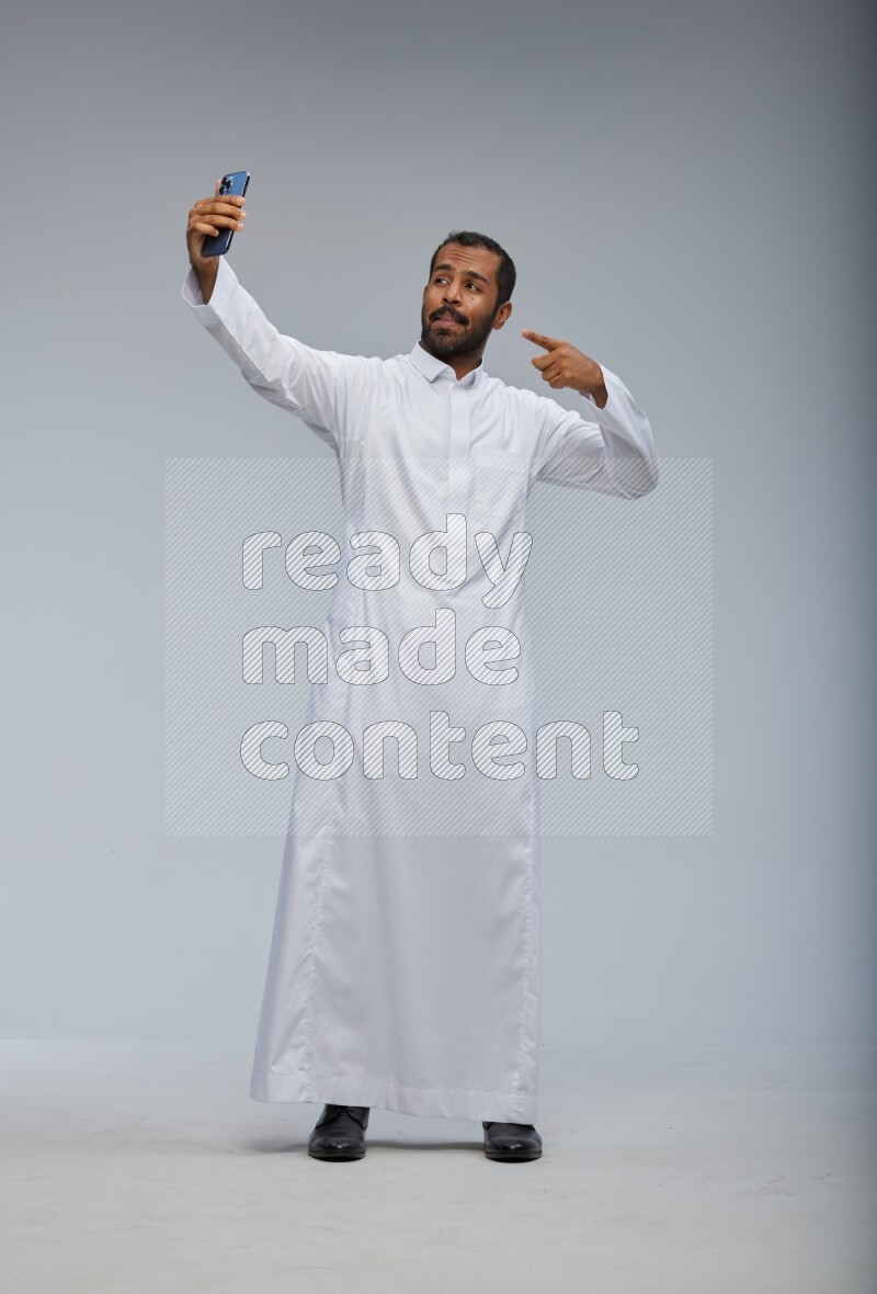 Saudi man wearing Thob standing taking selfie on Gray background
