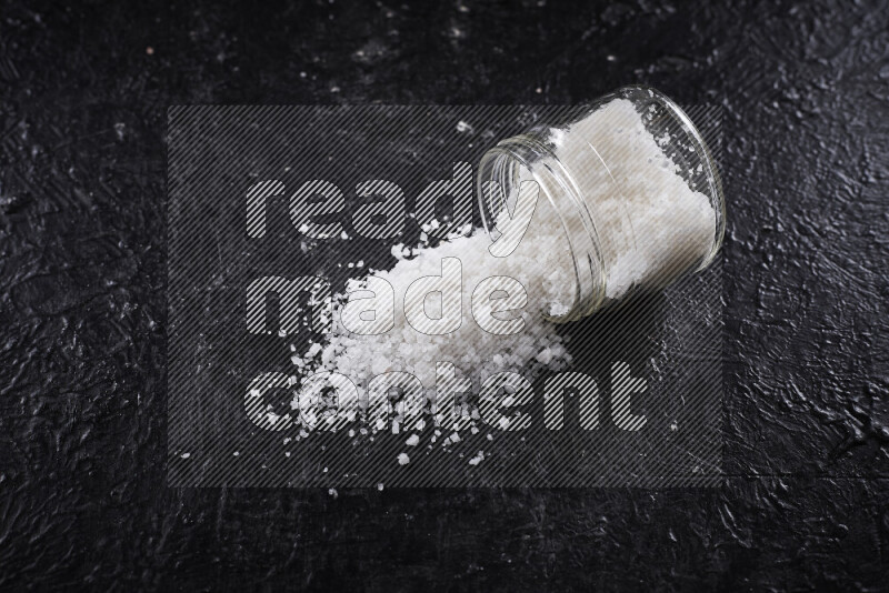 A glass jar full of coarse sea salt crystals on black background