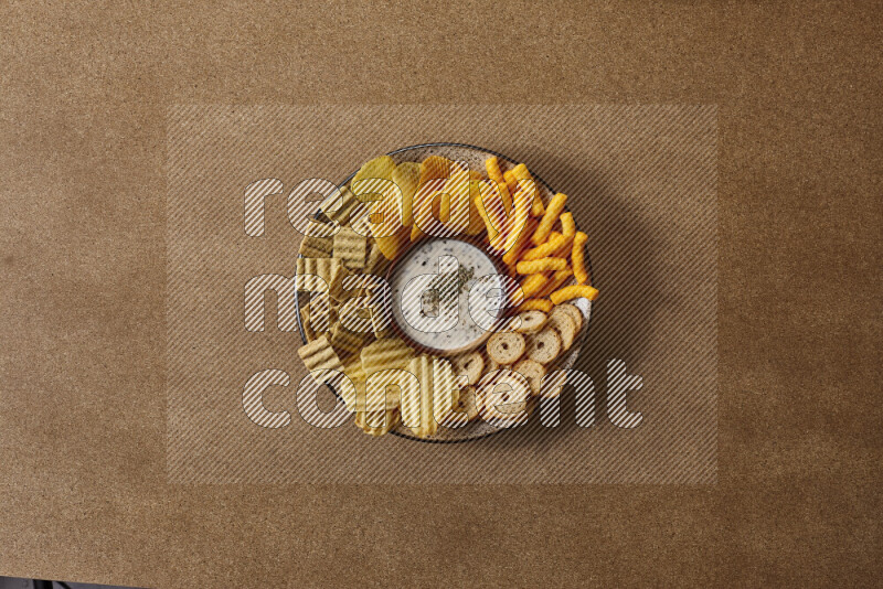 Assorted snacks on a pottery plate with a dipping on brown background