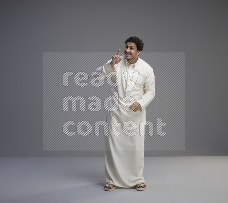 A Saudi man standing wearing thob interacting with the camera on gray background