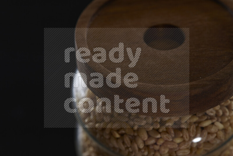 Hulled wheat in a glass jar on black background