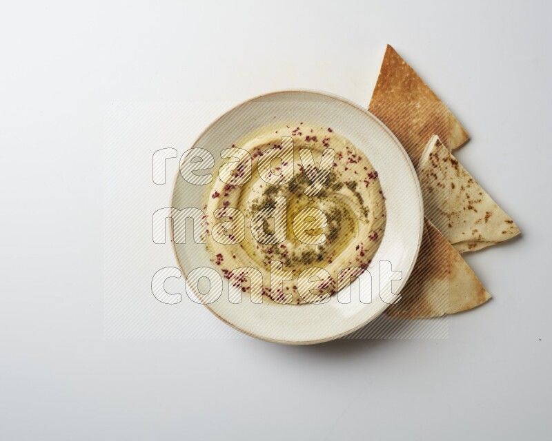 Hummus in a pottry plate garnished with zaatr & sumak on a white background