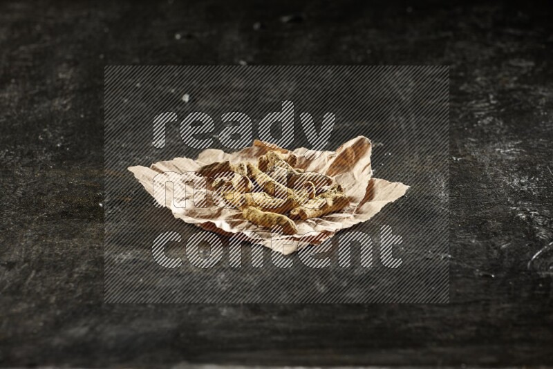 Dried turmeric whole fingers in a crumpled piece of paper on textured black flooring