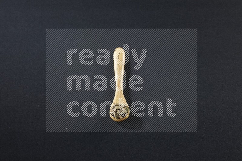 ملعقة خشبية ممتلئة بالهيل على خلفية سوداء