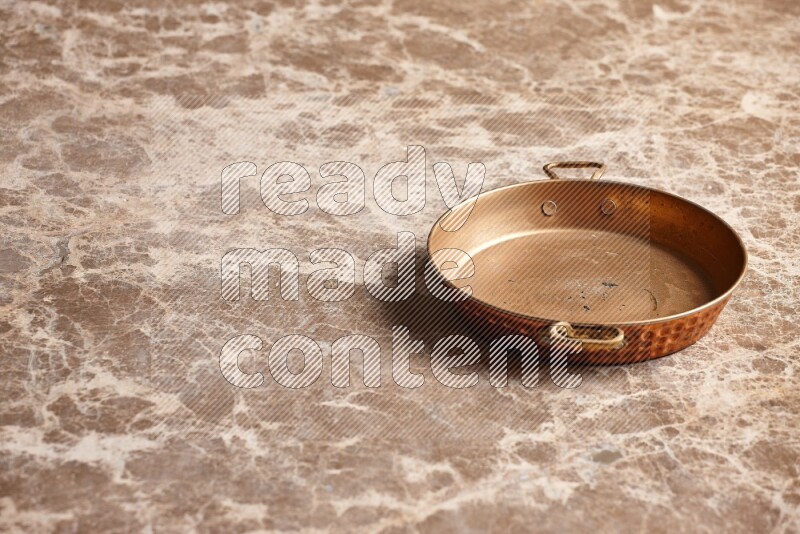 A small copper pan on beige marble background