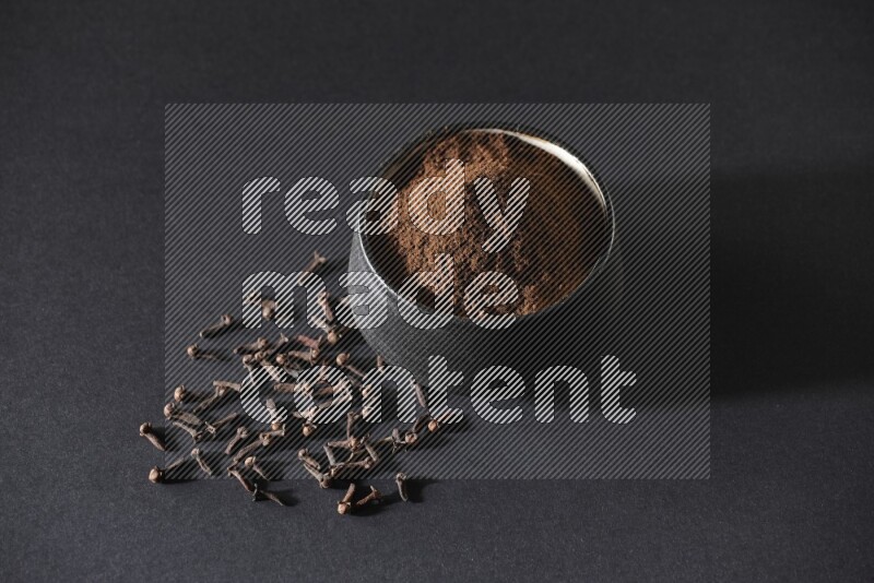 وعاء فخاري أسود ممتلئ ببودرة القرنفل وحبوب القرنفل على خلفية سوداء