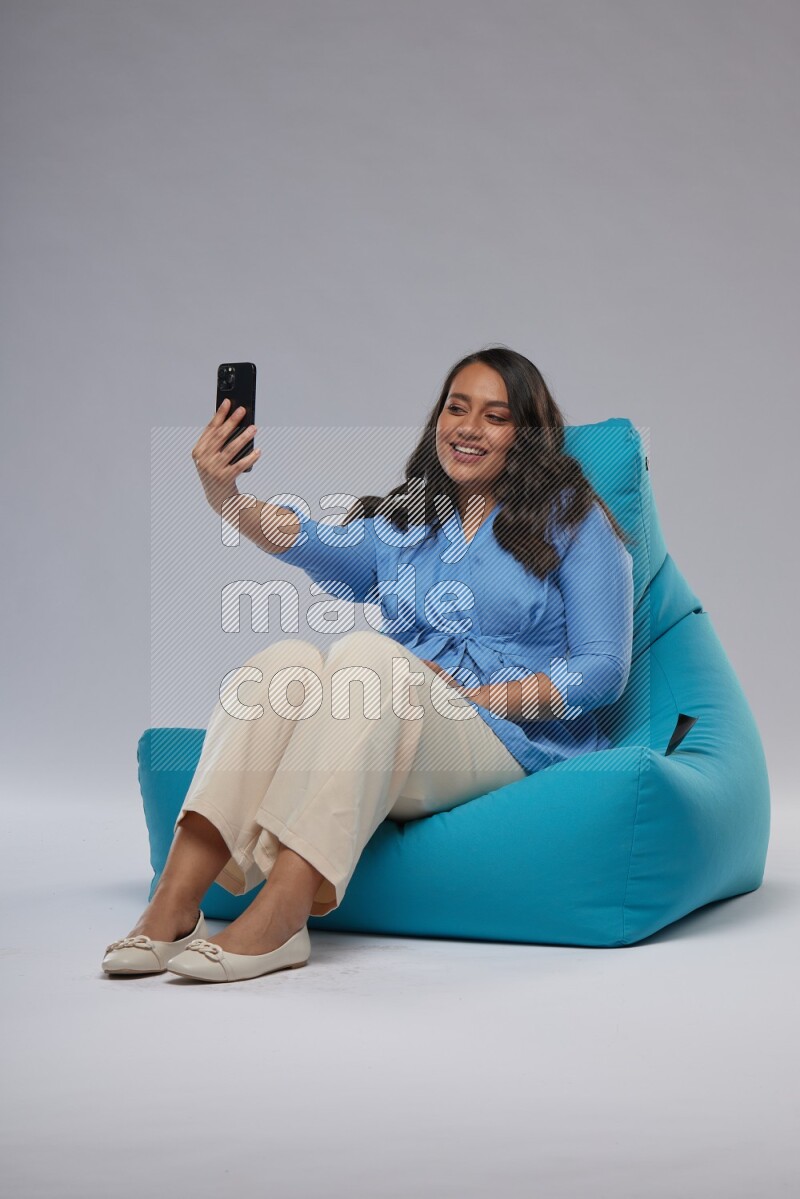 A woman sitting on a blue beanbag and taking selfie