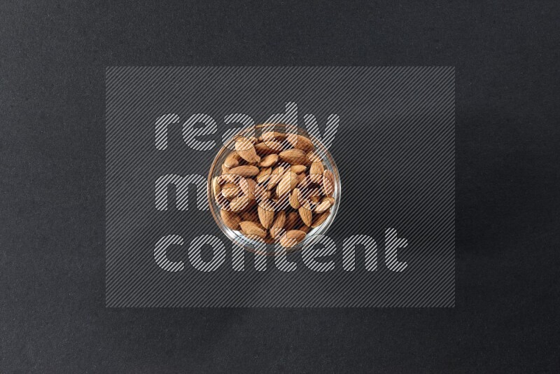 A glass bowl full of peeled almonds on a black background in different angles