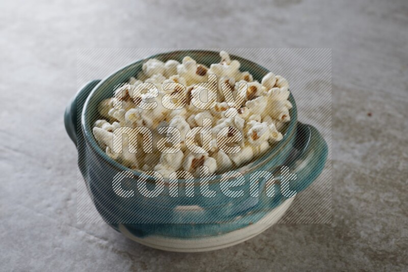 popcorn in a multi-colored handheld ceramic bowl on a grey textured countertop