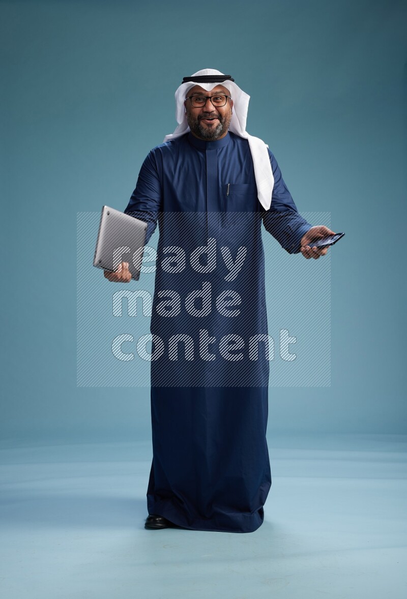 Saudi Man with shimag Standing texting on phone on blue background