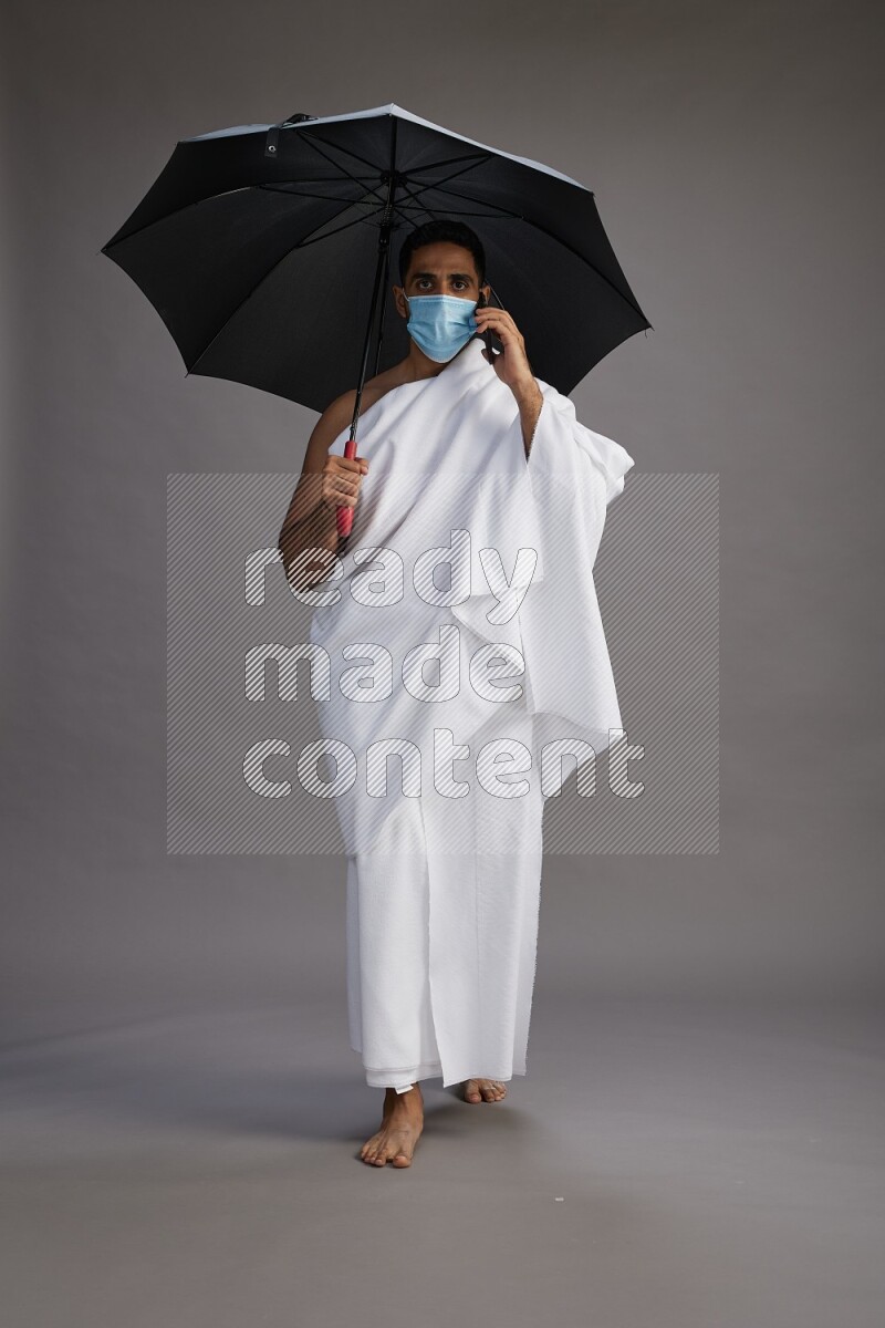 A man wearing Ehram and mask Standing holding umbrella on gray background on gray background