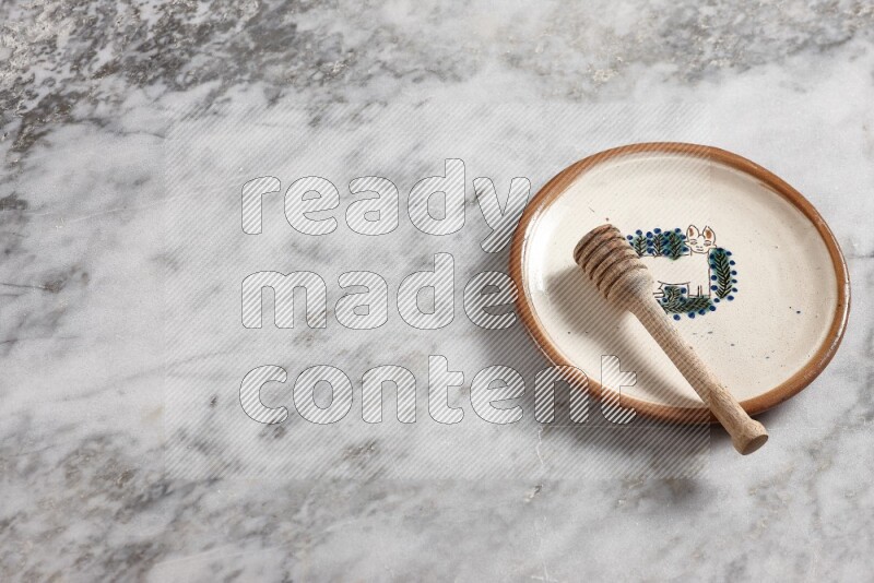 Decorative pottery plate with wooden honey dipper in it on grey marble background
