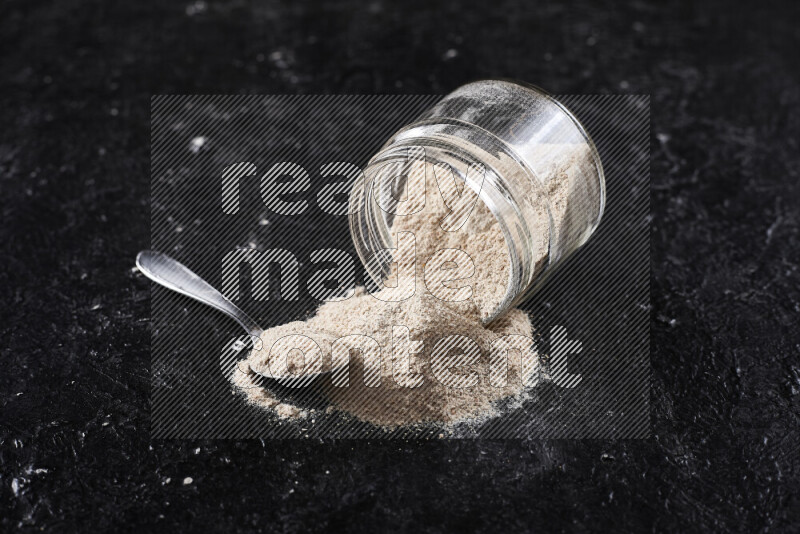 A glass jar full of onion powder flipped with some spilling powder on black background