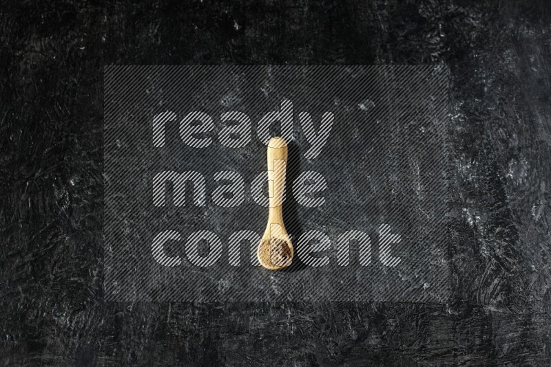A wooden spoon full of allspice powder on a textured black flooring