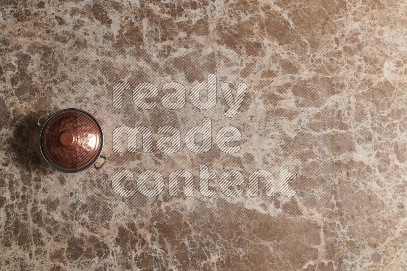 A small copper pot on beige marble background