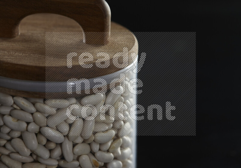 White beans in a glass jar on black background