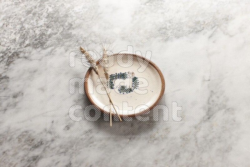 Wheat stalks on decorative pottery plate on grey marble background
