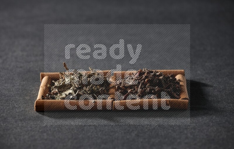 2 squares of cinnamon sticks full of cloves and dried basil on black flooring