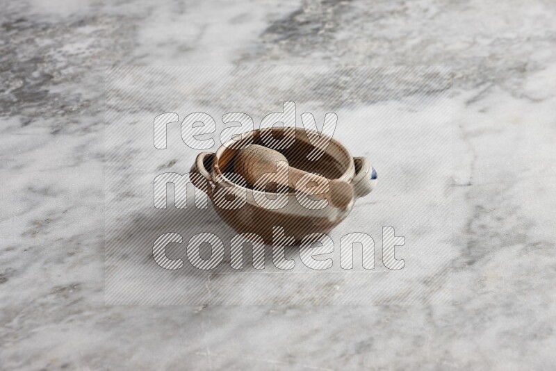 Multicolored pottery bowl with wooden honey dipper in it on grey marble background