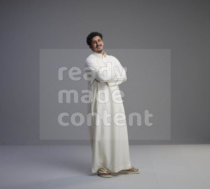 A Saudi man standing wearing thob interacting with the camera on gray background