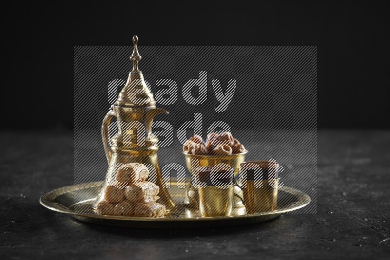 Oriental sweets with dates and a drink on a metal tray in a dark setup