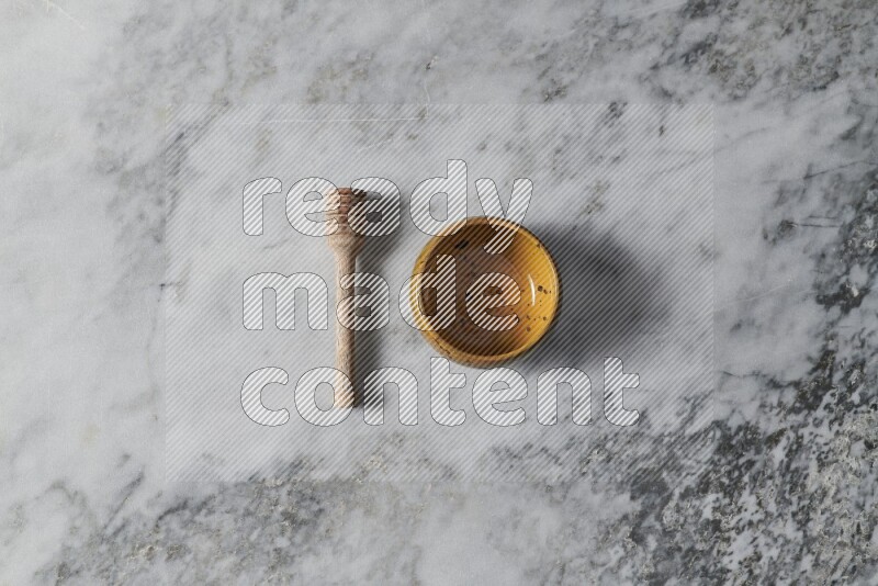 Multicolored pottery bowl with wooden honey dipper on the side on grey marble background