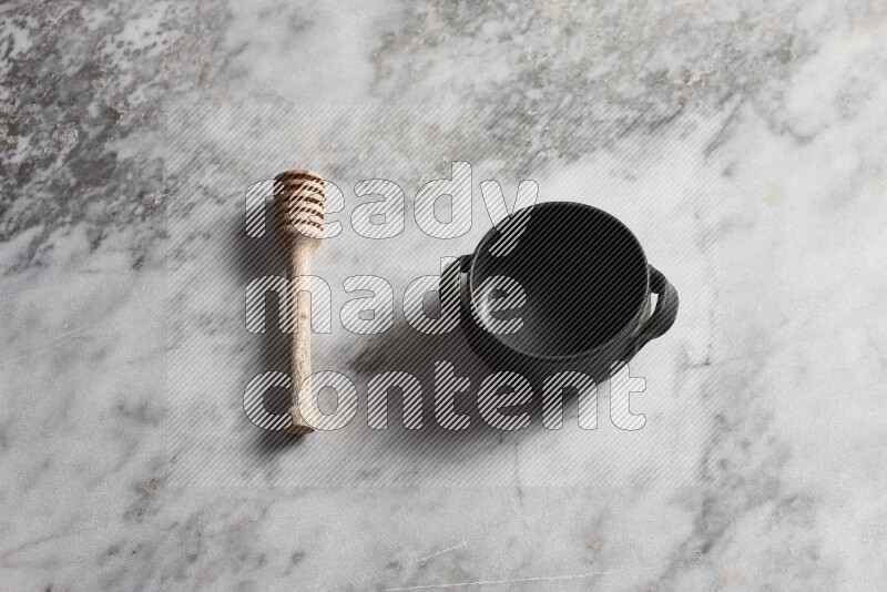 Black pottery bowl with wooden honey dipper on the side on grey marble background