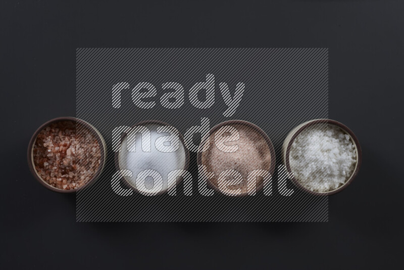 4 pottery bowls filled with himalayan salt and white salt on black background