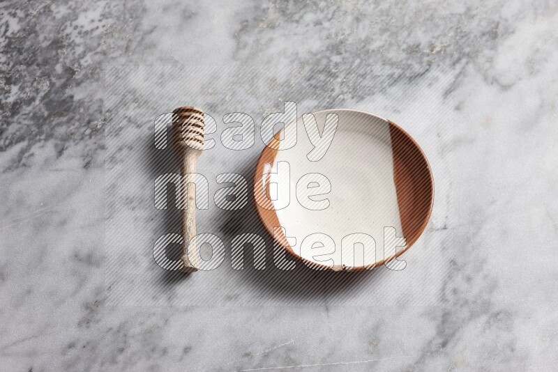 Multicolored pottery plate with wooden honey dipper on the side on grey marble background