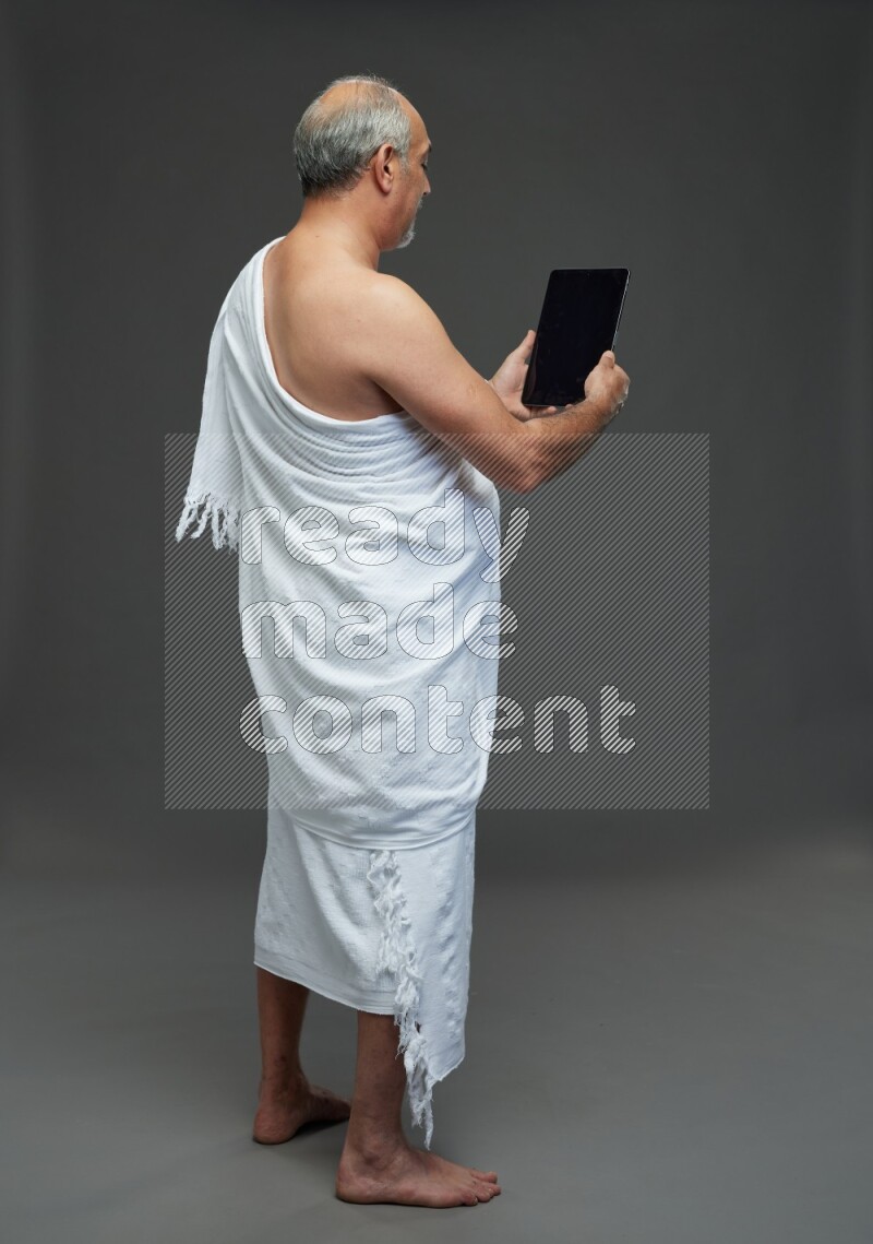 A man wearing Ehram Standing working on tablet on gray background