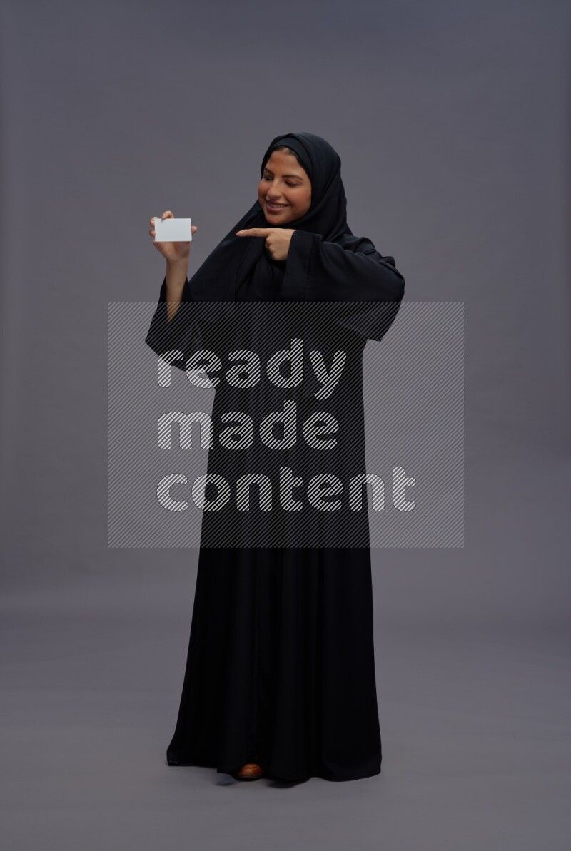 Saudi woman wearing Abaya standing holding ATM card on gray background
