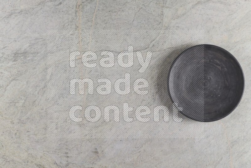 A circular black pottery plate on grey marble background