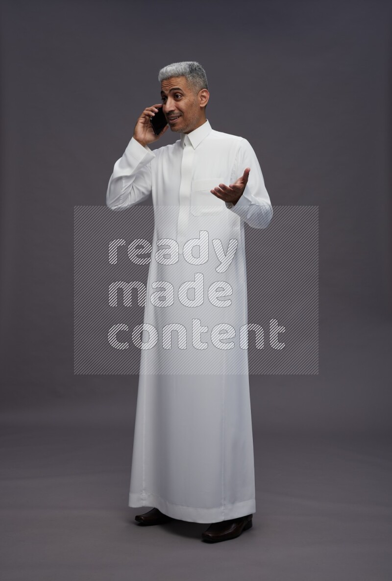 Saudi man wearing thob standing talking on phone on gray background