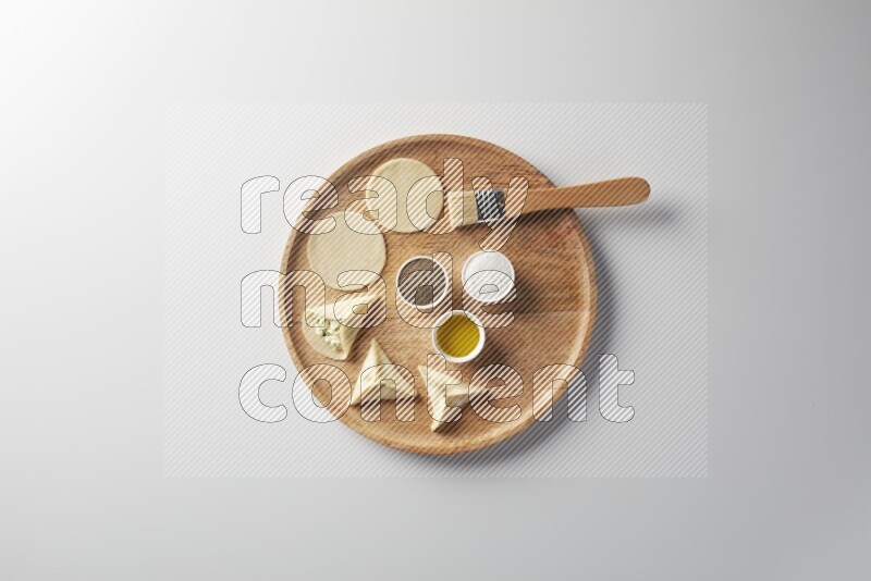 two closed sambosas and one open sambosa filled with cheese while salt, black pepper and oil with oil brush aside in a wooden dish on a white background