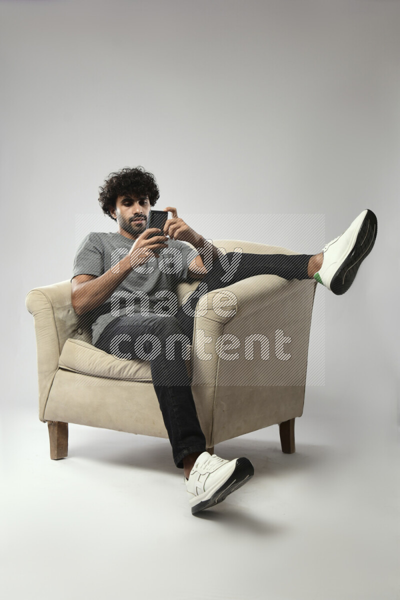 A man wearing casual sitting on a chair texting on the phone on white background