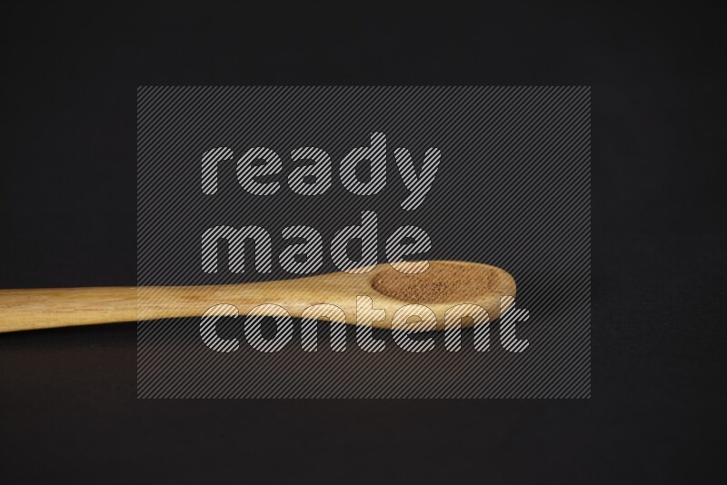 Cinnamon powder in a wooden spoon on a black background